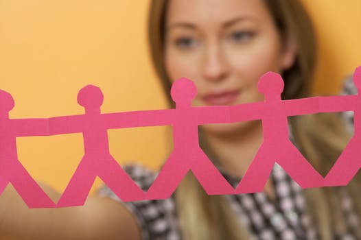 Close-up of a young woman holding pink paper chain figures against an orange background.